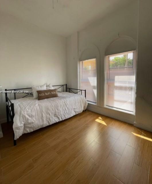A bedroom with a daybed, wood-look tile flooring, and two arched windows with blinds — 7149 Bay Dr # 2, Miami Beach FL 33141, MIAMI BEACH, FL