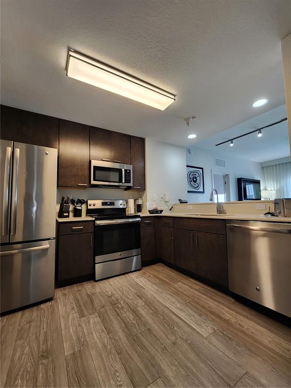 A kitchen features dark wood cabinets, stainless steel appliances, and light wood-look flooring — 14501 GROVE RESORT AVENUE UNIT 3737, WINTER GARDEN, FL