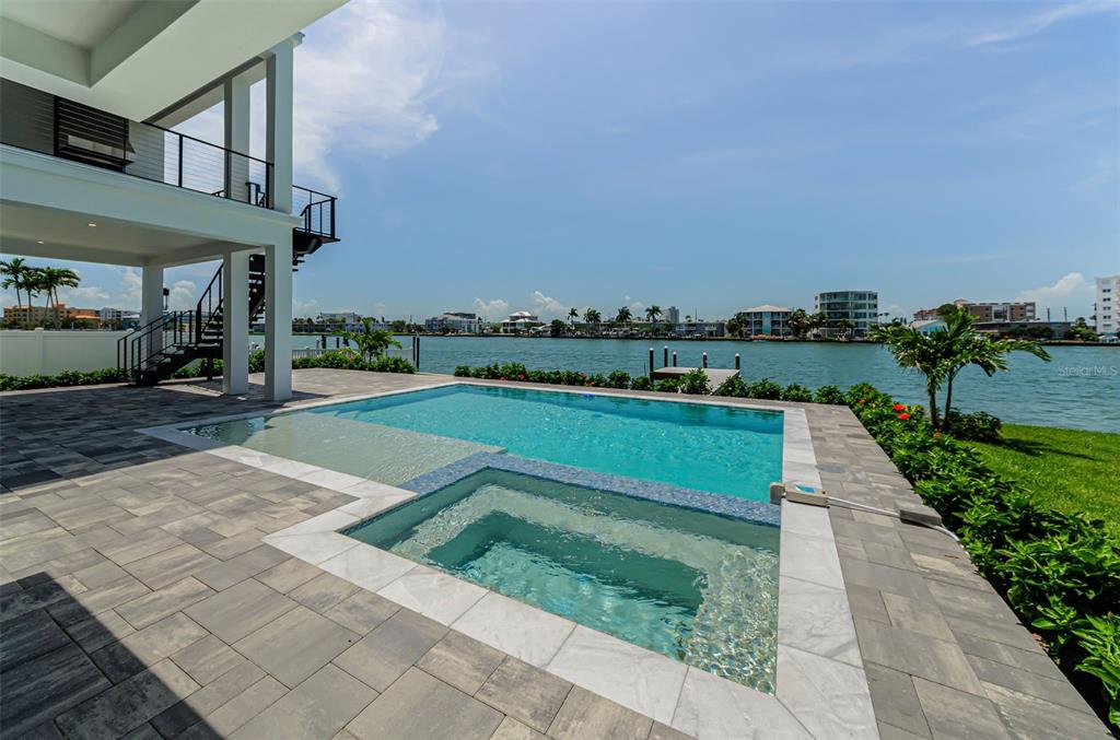 A modern swimming pool and spa overlook a waterfront view from a paved patio — 43 DOLPHIN DRIVE, TREASURE ISLAND, FL