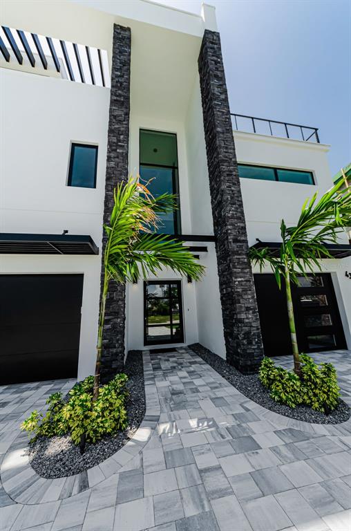 A modern white house exterior features dark stone pillars, black garage doors, and palm trees — 43 DOLPHIN DRIVE, TREASURE ISLAND, FL