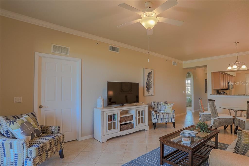 A living room features tile floors, a ceiling fan, a television console, and patterned armchairs — 8205 GRAND ESTUARY TRAIL UNIT 105, BRADENTON, FL