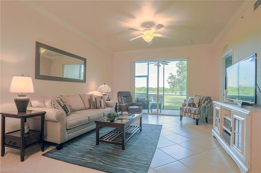 A living room features a beige sofa, patterned armchair, coffee table, and a view of water — 8205 GRAND ESTUARY TRAIL UNIT 105, BRADENTON, FL