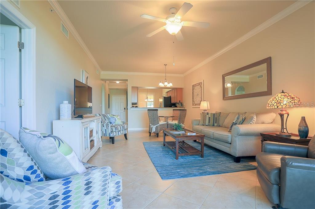 A living room with tile floors, a beige sofa, a blue rug, and a ceiling fan — 8205 GRAND ESTUARY TRAIL UNIT 105, BRADENTON, FL