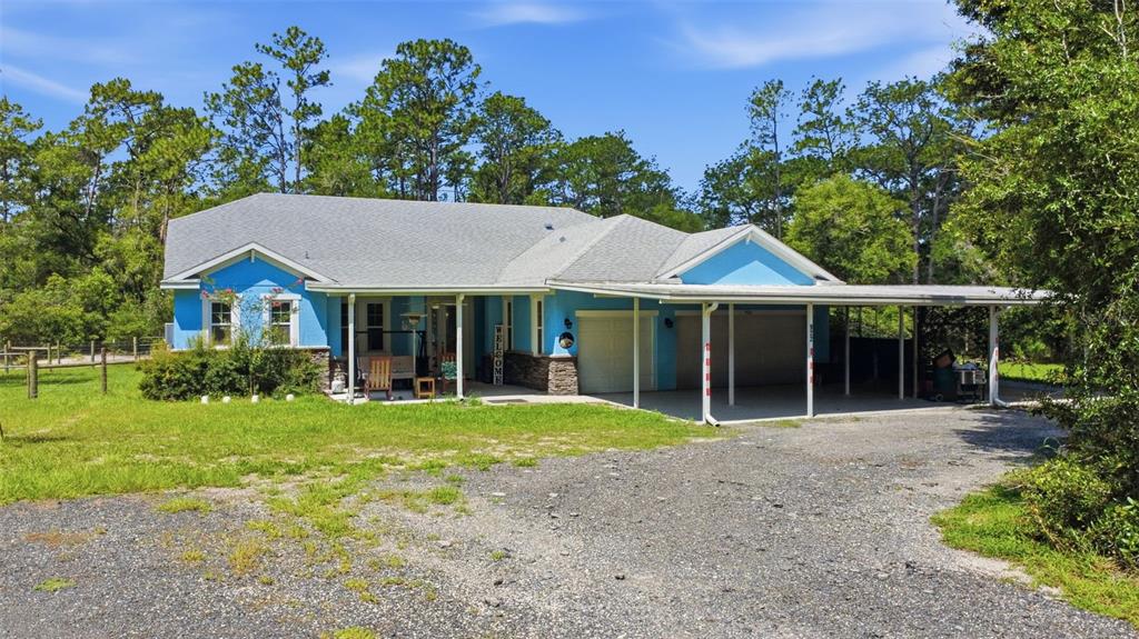 A blue single-story house with a gravel driveway, attached garage, and a large metal carport — 922 VOLUSIA TIMBER COURT, LAKE HELEN, FL