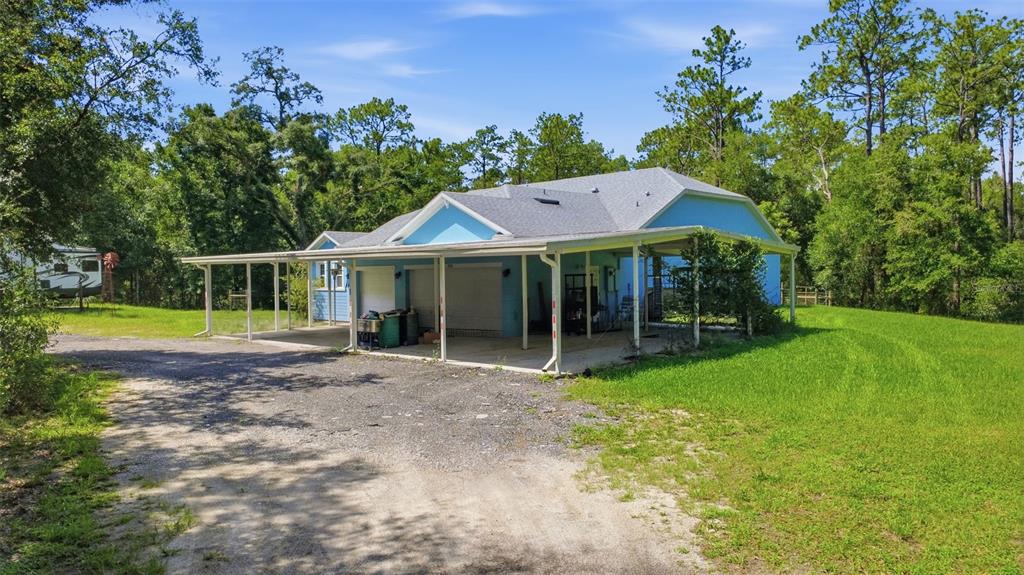 A light blue house with a large attached carport sits on a grassy, wooded lot — 922 VOLUSIA TIMBER COURT, LAKE HELEN, FL
