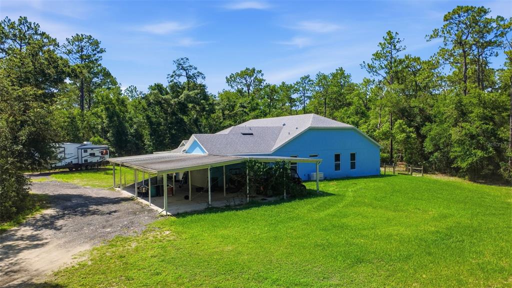 A blue house with a large attached carport sits on a grassy lot near trees — 922 VOLUSIA TIMBER COURT, LAKE HELEN, FL