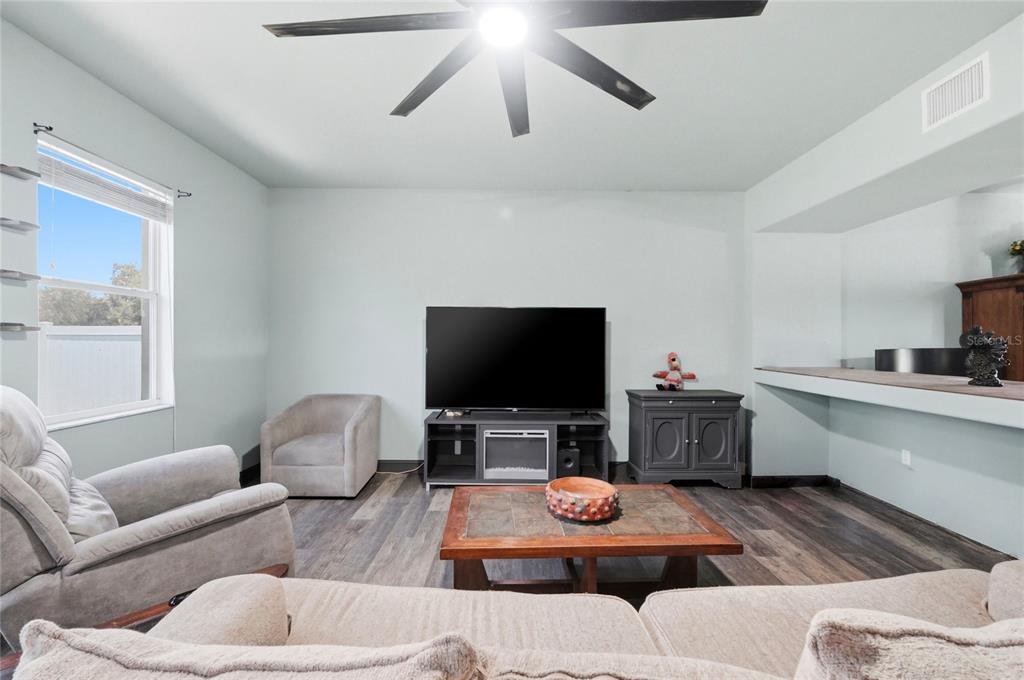 A living room features a television on a stand, gray seating, and wood-look flooring — 2203 BLACKWOOD DRIVE, MULBERRY, FL