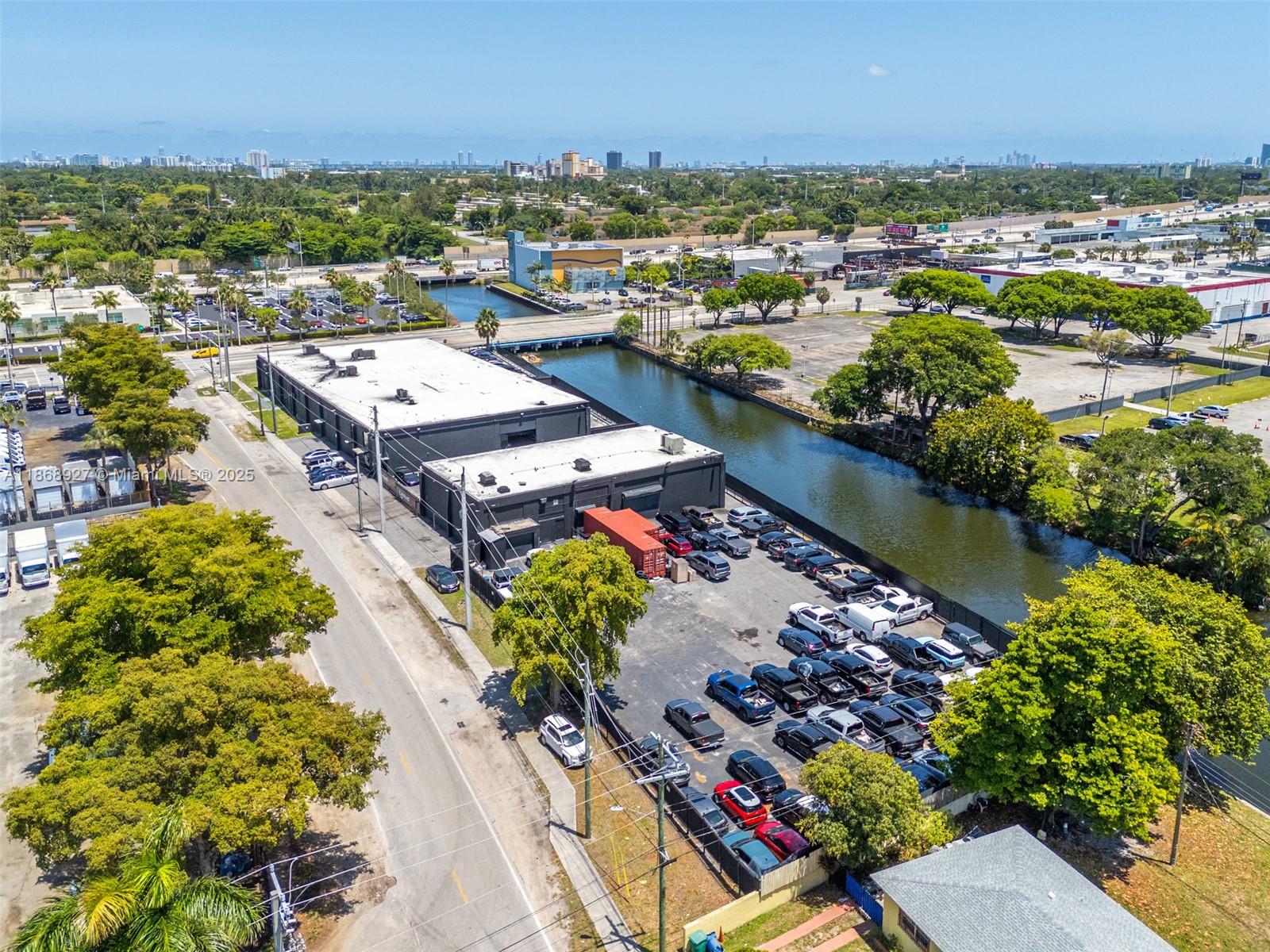 An aerial view shows a black industrial building with a parking lot beside a canal — 8700 NW 7th Ave, Miami FL 33150, MIAMI, FL