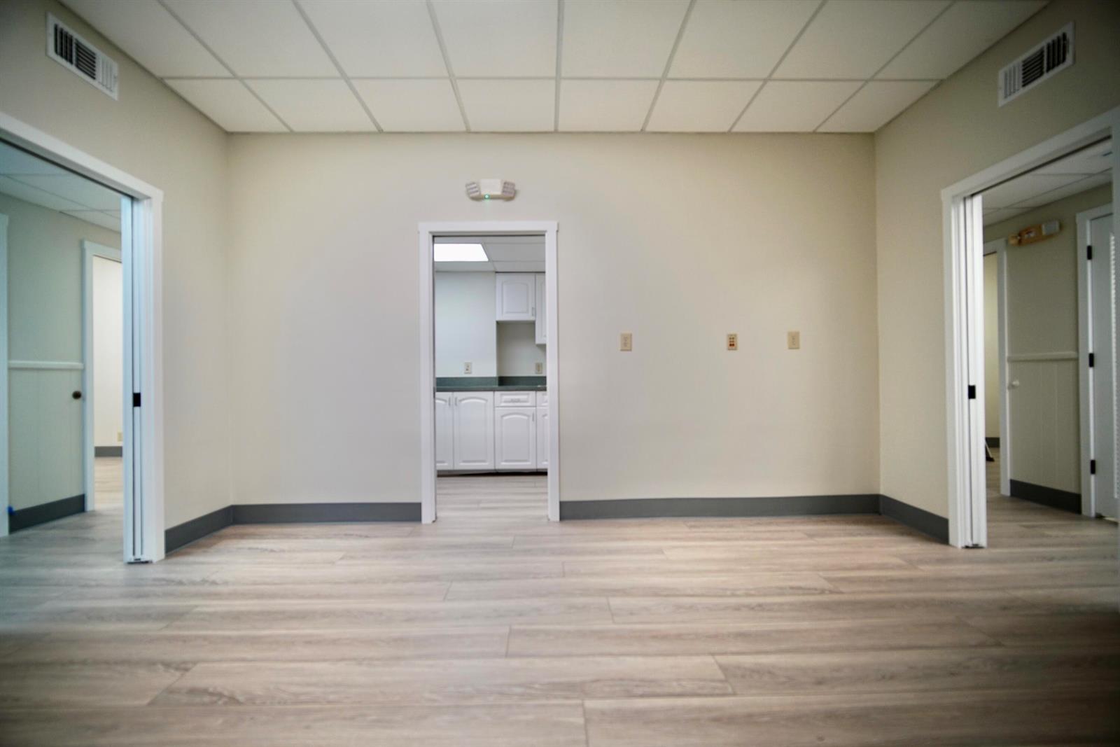 An empty room with light wood-look flooring, beige walls, a drop ceiling, and three doorways — 2231 NE 25th Avenue # 1, Pompano Beach FL 33062, POMPANO BEACH, FL
