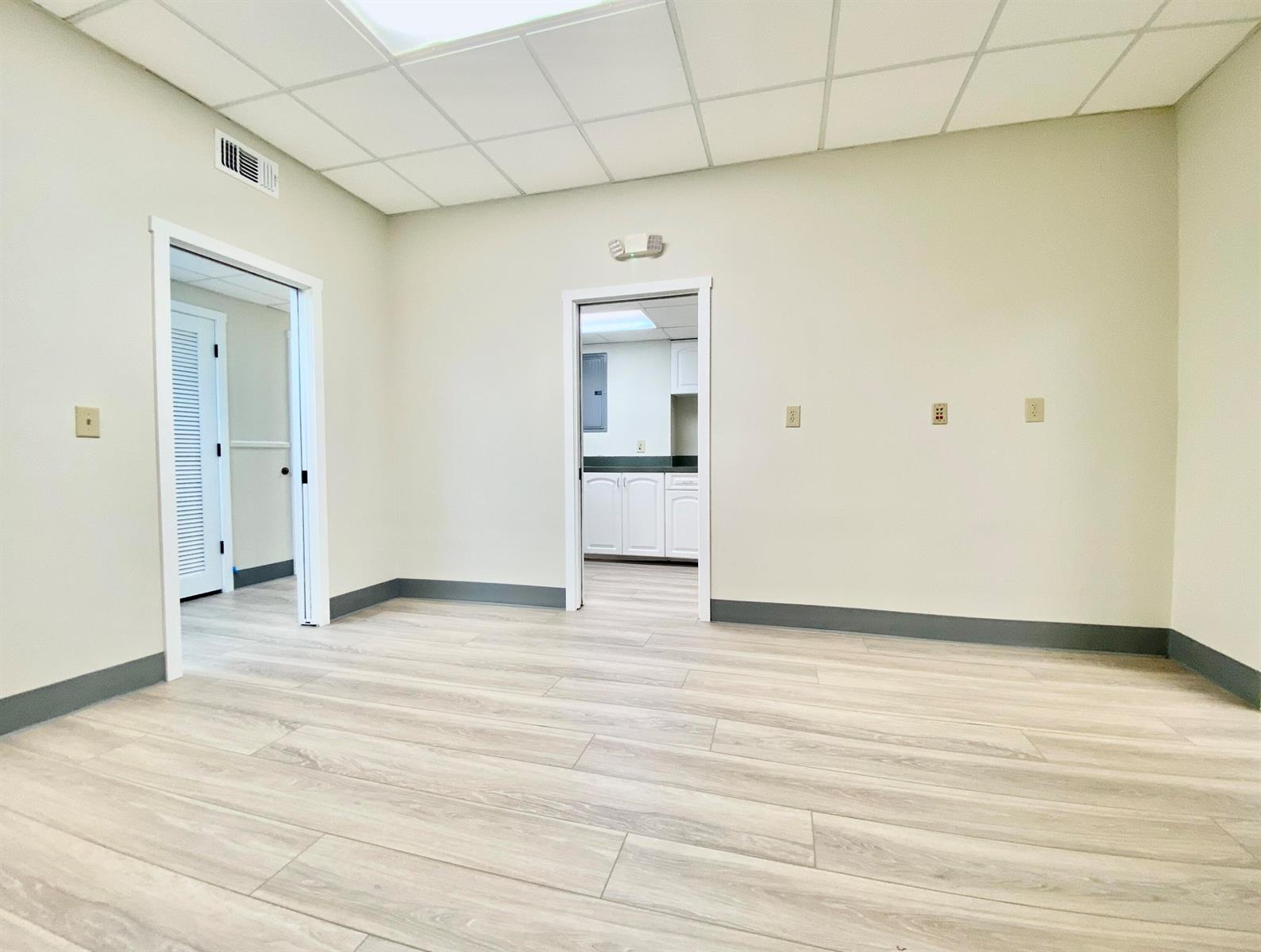An empty room with light wood-look flooring, beige walls, and two doorways leading to other rooms — 2231 NE 25th Avenue # 1, Pompano Beach FL 33062, POMPANO BEACH, FL