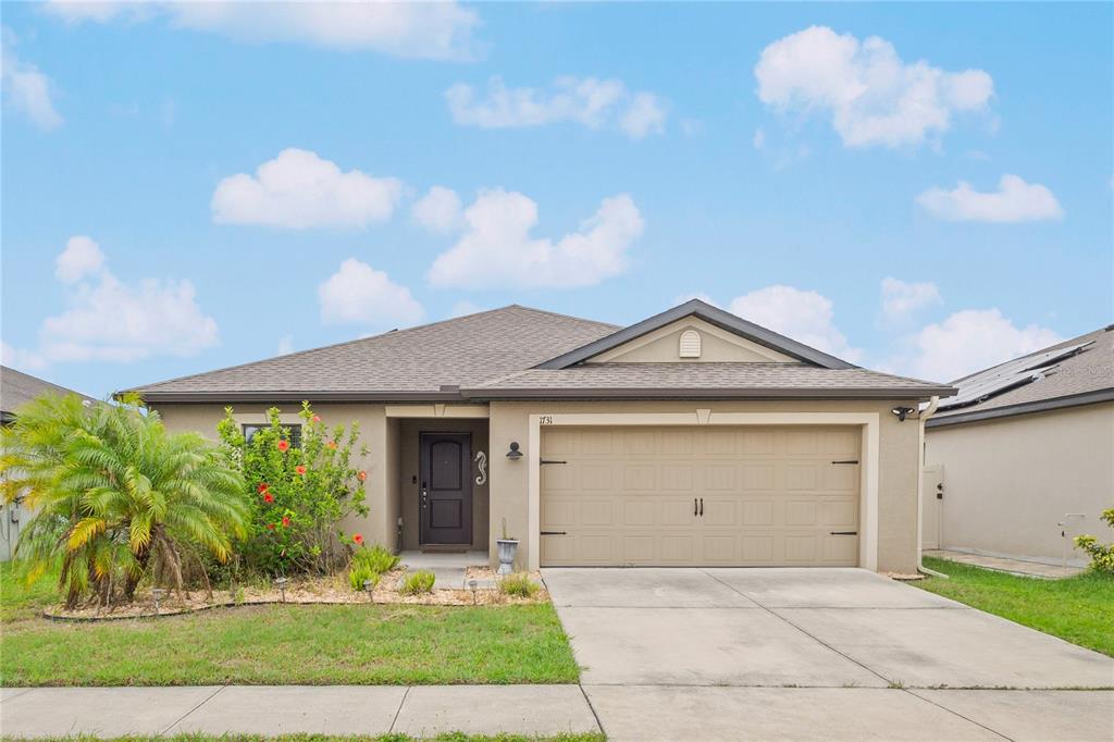 A single-story house with a beige stucco exterior, a two-car garage, and a palm tree — 1731 CHATHAM GREEN CIRCLE, RUSKIN, FL