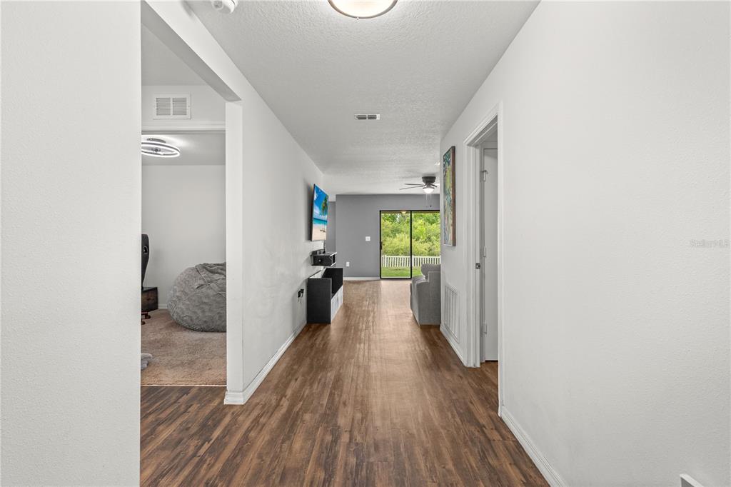 A hallway with wood-look flooring leads to a living area with a sliding glass door — 1731 CHATHAM GREEN CIRCLE, RUSKIN, FL