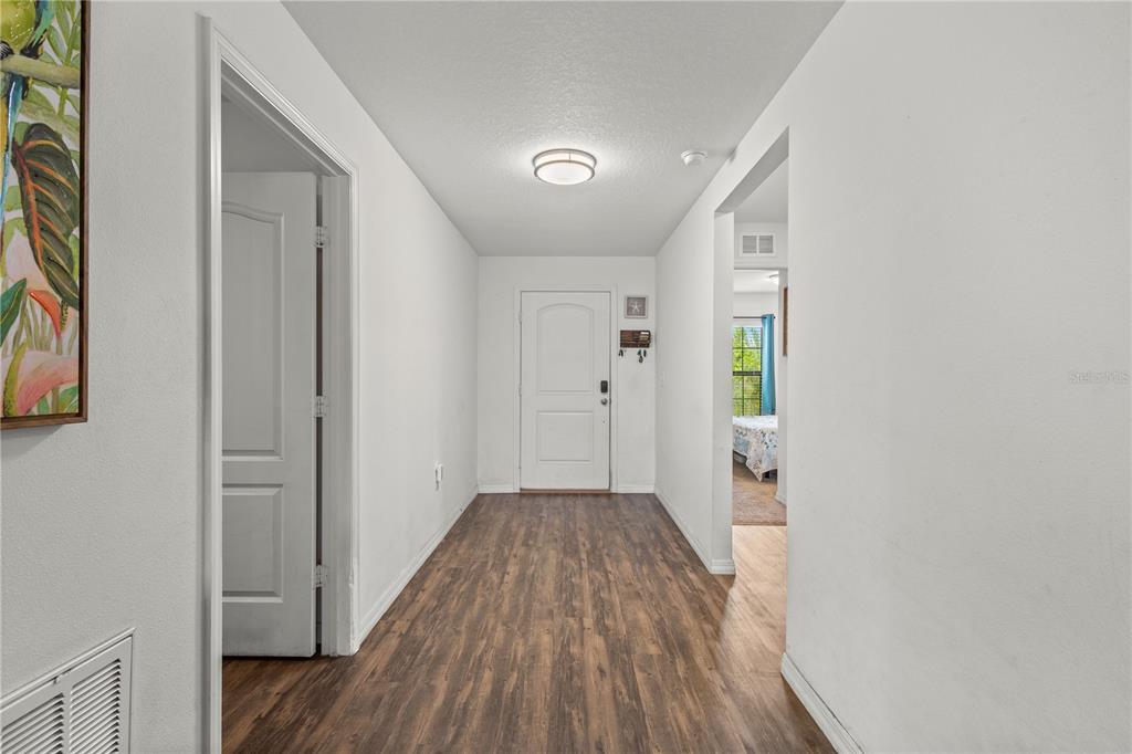 A hallway with wood-look flooring leads to a white front door and an adjacent room — 1731 CHATHAM GREEN CIRCLE, RUSKIN, FL