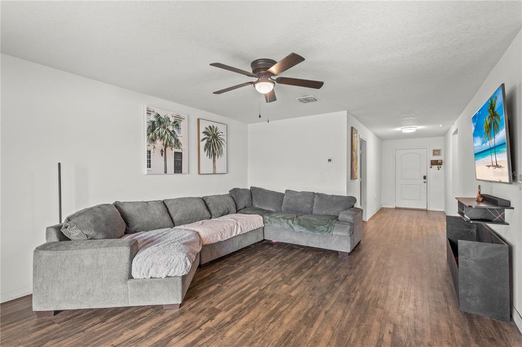 A living room features a large gray sectional sofa, wood-look flooring, and a wall-mounted television — 1731 CHATHAM GREEN CIRCLE, RUSKIN, FL