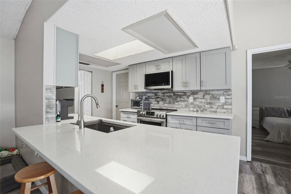 A kitchen features gray cabinets, a white quartz island, and a brick-style backsplash — 13032 LOLA DRIVE, SPRING HILL, FL
