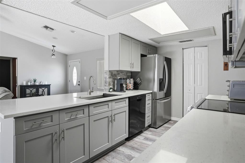 A kitchen features gray cabinets, white countertops, stainless steel appliances, and a skylight — 13032 LOLA DRIVE, SPRING HILL, FL