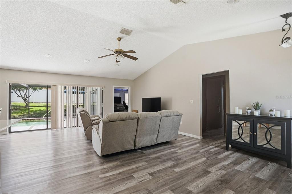 A living room with wood-look flooring, a vaulted ceiling, a sectional sofa, and sliding glass doors — 13032 LOLA DRIVE, SPRING HILL, FL