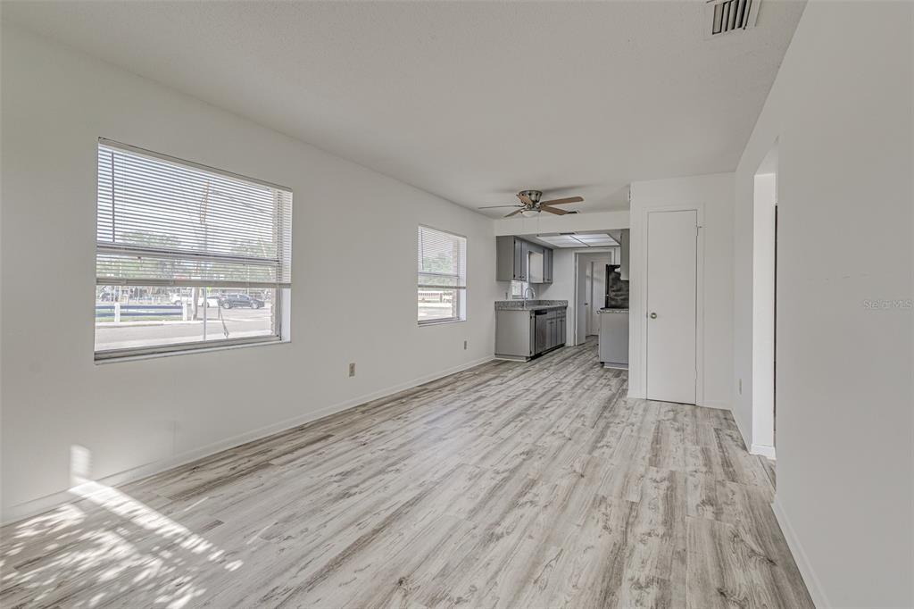 An open-concept living area features light wood-look flooring, white walls, and a view into the kitchen — 401 BIG CEDAR WAY UNIT A, BRANDON, FL