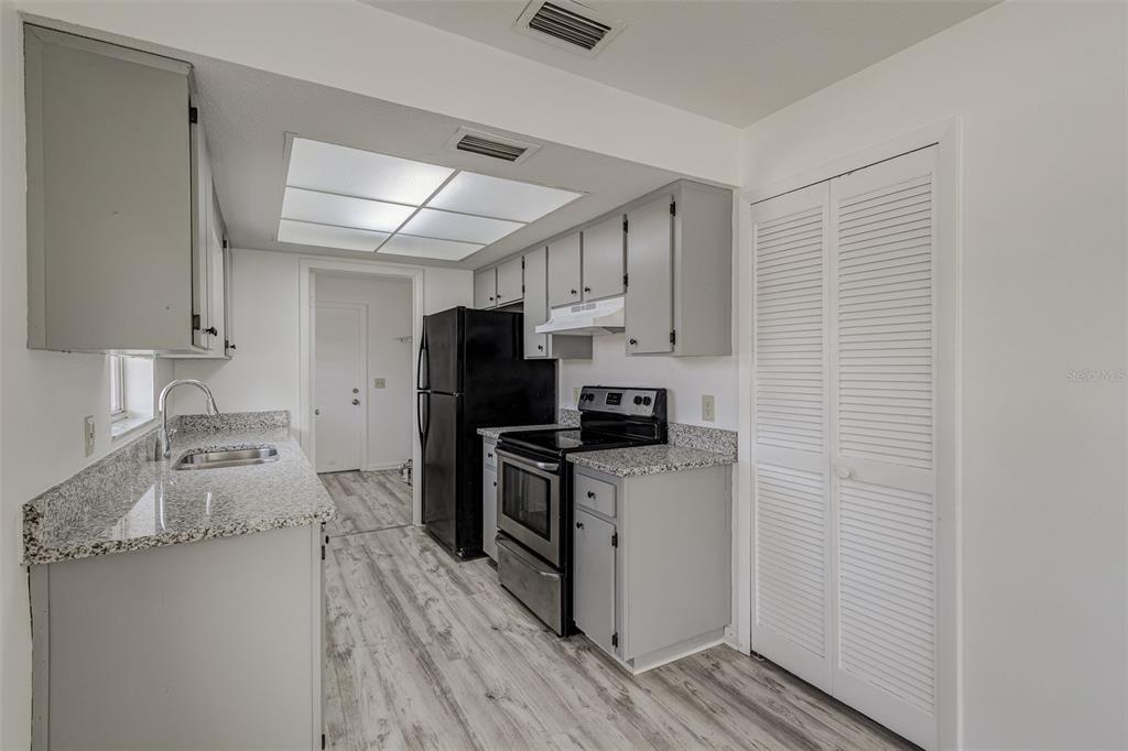 A galley-style kitchen features gray cabinets, granite countertops, black appliances, and light wood-look flooring — 401 BIG CEDAR WAY UNIT A, BRANDON, FL