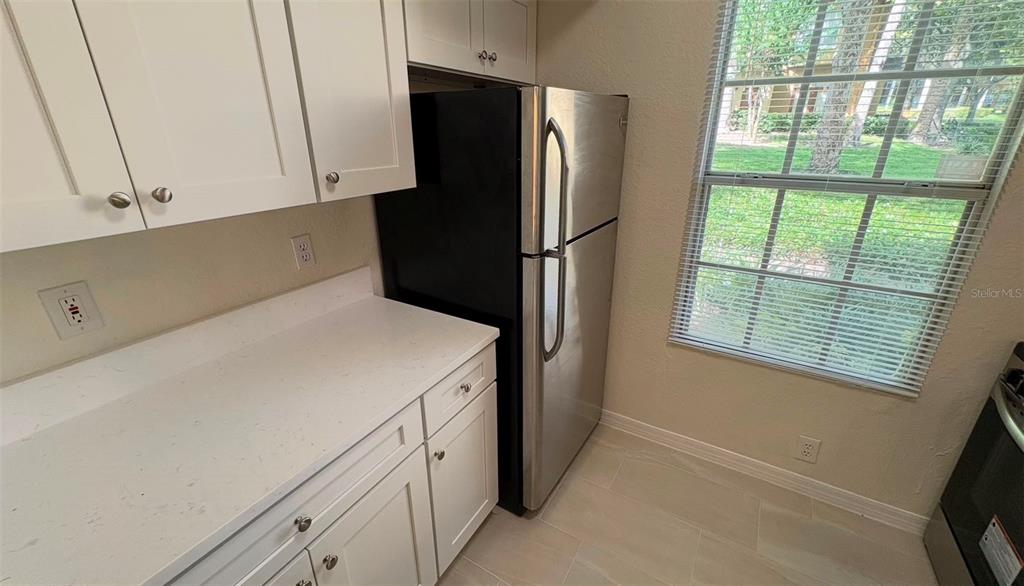 A kitchen features white cabinets, a stainless steel refrigerator, and a window with blinds — 6348 RALEIGH STREET UNIT 1304, ORLANDO, FL