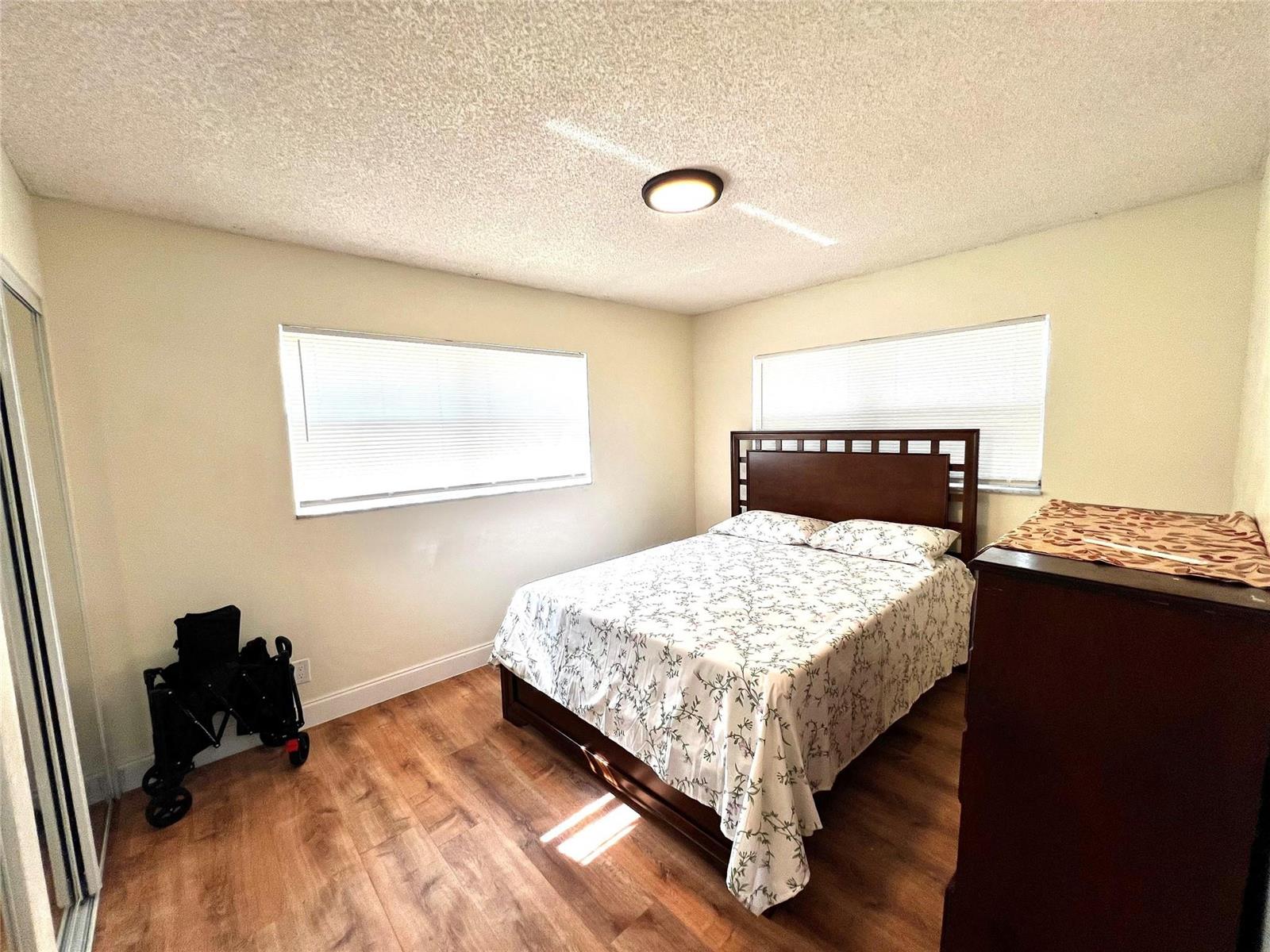A bedroom features wood-look flooring, a dark wood bed frame, and two windows with blinds — 3080 Holiday Springs Boulevard # 301, Margate FL 33063, MARGATE, FL