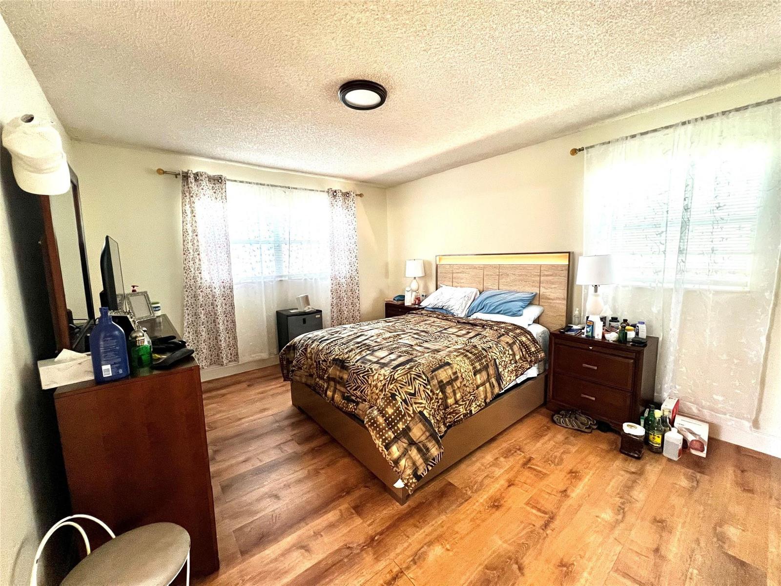 A bedroom features wood-look flooring, a bed with a patterned comforter, and two windows — 3080 Holiday Springs Boulevard # 301, Margate FL 33063, MARGATE, FL