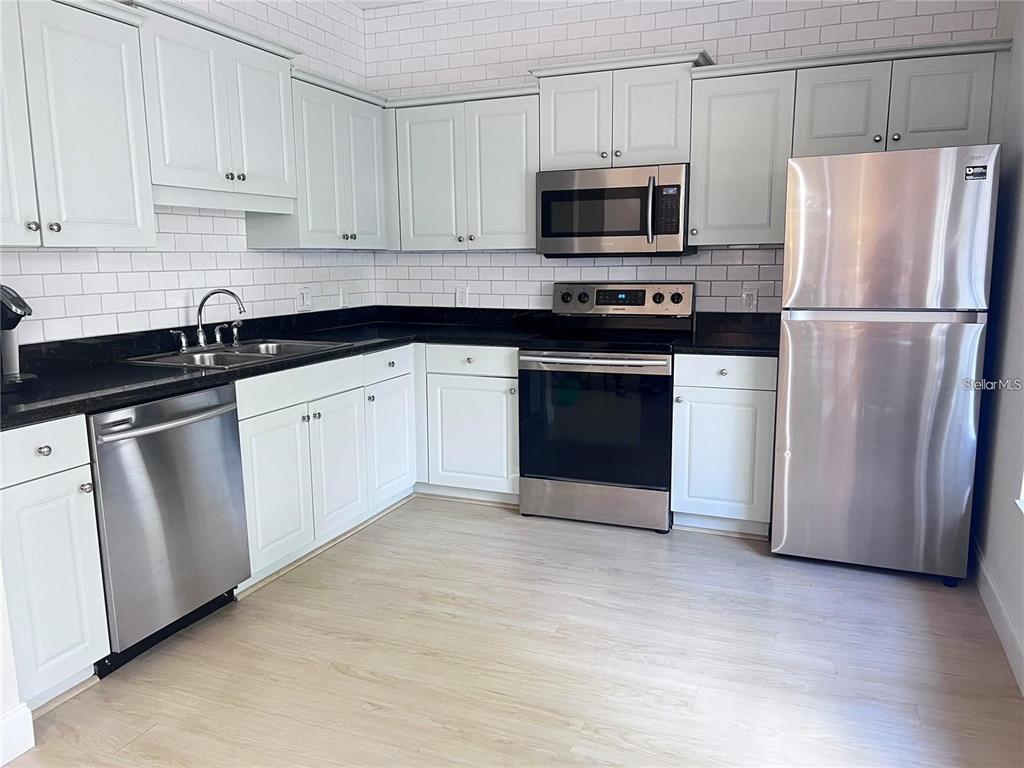 A kitchen features white cabinets, stainless steel appliances, black countertops, and white subway tile backsplash — 7658 PLANTATION CIRCLE, BRADENTON, FL