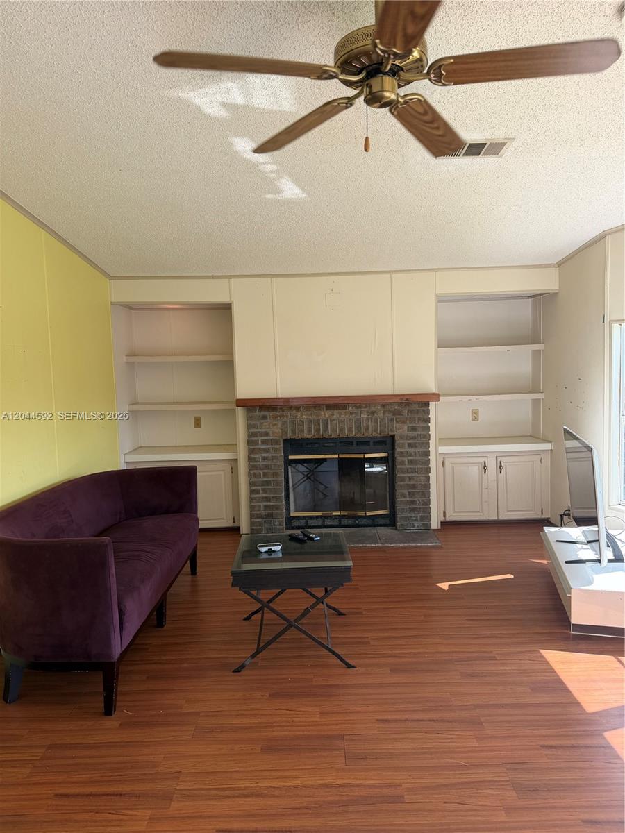 A living room features a brick fireplace, built-in shelving, a purple sofa, and wood flooring — 1233 SW 130 Ave # 1233, Miami FL 33184, MIAMI, FL