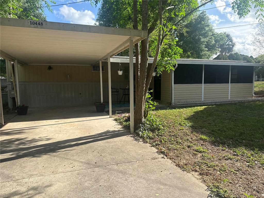 A single-story home features a concrete driveway, a metal carport, and a screened-in porch — 10448 SE 148TH PLACE, SUMMERFIELD, FL