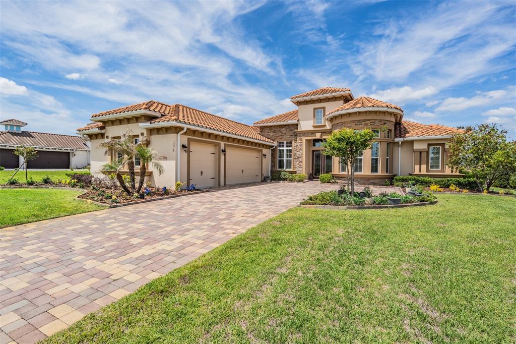 A single-story Mediterranean-style house with a tile roof, stone facade, and a paved driveway — 13915 CARRYBACK DRIVE, DADE CITY, FL