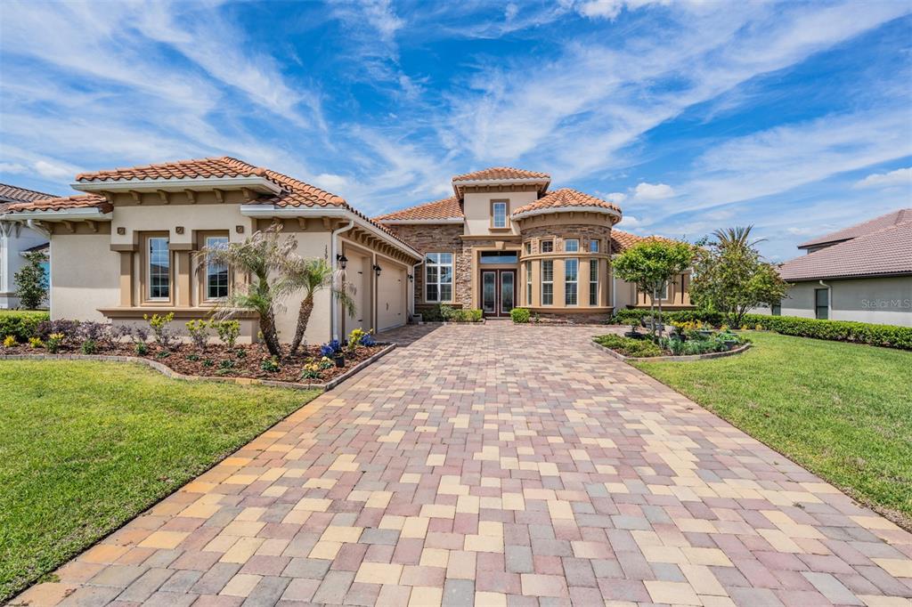 A single-story Mediterranean-style house with a paver driveway, stone accents, and a tile roof — 13915 CARRYBACK DRIVE, DADE CITY, FL