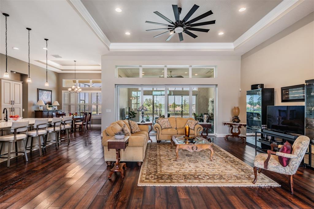 An open-concept living room and kitchen feature dark wood floors, a tray ceiling, and sliding doors — 13915 CARRYBACK DRIVE, DADE CITY, FL