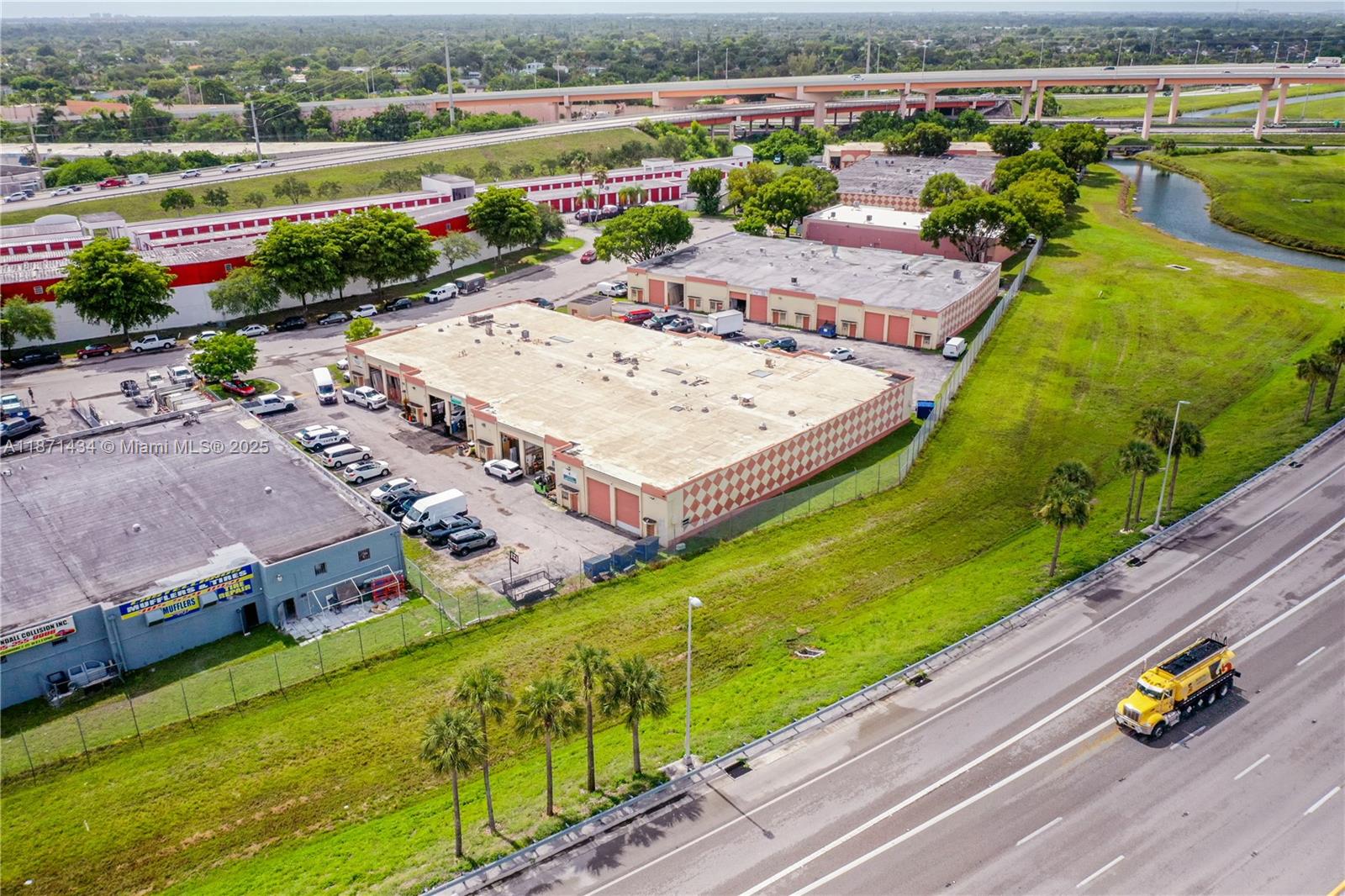 An aerial view shows commercial warehouse buildings with parking lots near a highway and canal — 12300 SW 117 CT, FL 33186, FL