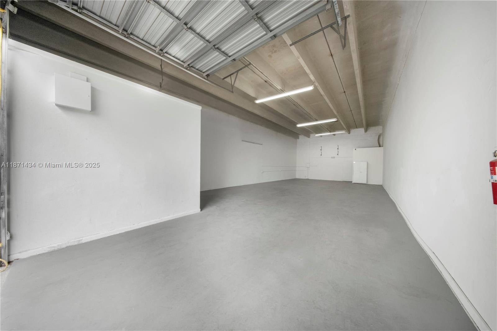 An empty industrial warehouse space features white walls, a gray concrete floor, and exposed ceiling beams — 12300 SW 117 CT, FL 33186, FL
