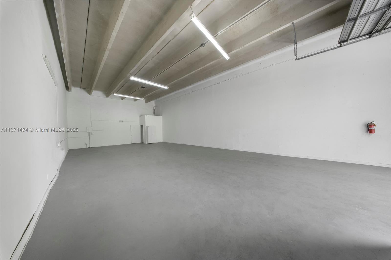 An empty industrial warehouse space features white walls, a gray concrete floor, and exposed ceiling beams — 12300 SW 117 CT, FL 33186, FL