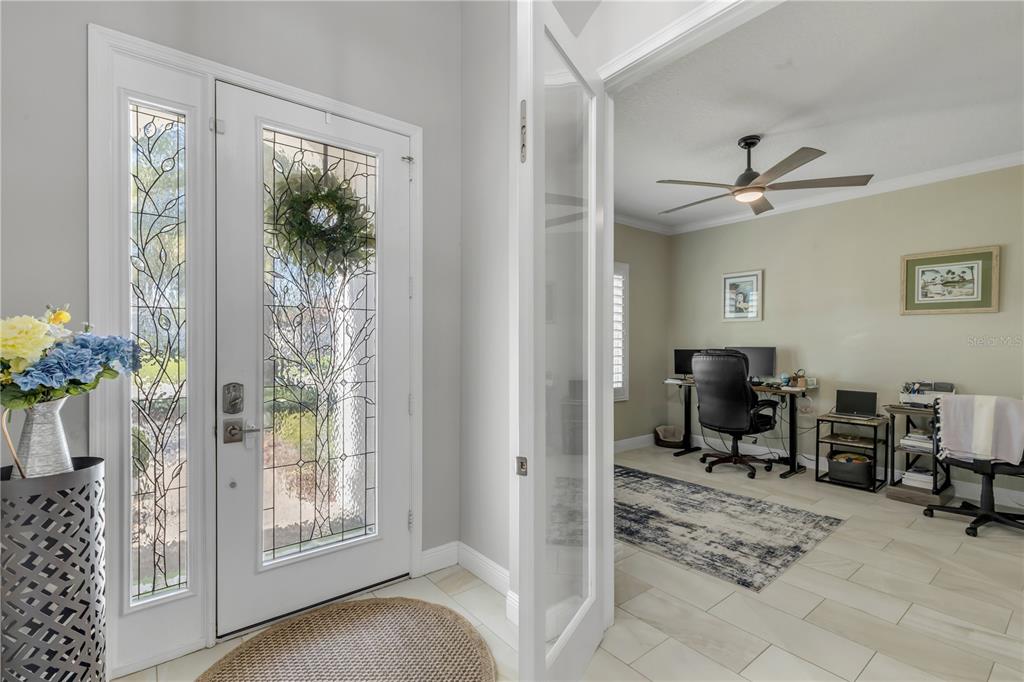 A white front door with decorative glass opens into a home office with tile flooring — 3029 ISOLA BELLA BOULEVARD, MOUNT DORA, FL