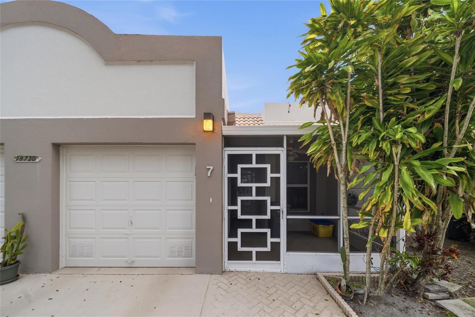 A single-story home exterior features a white garage door, a screened entryway, and landscaping — 18730 Stewart Circle # 7, Boca Raton FL 33496, BOCA RATON, FL