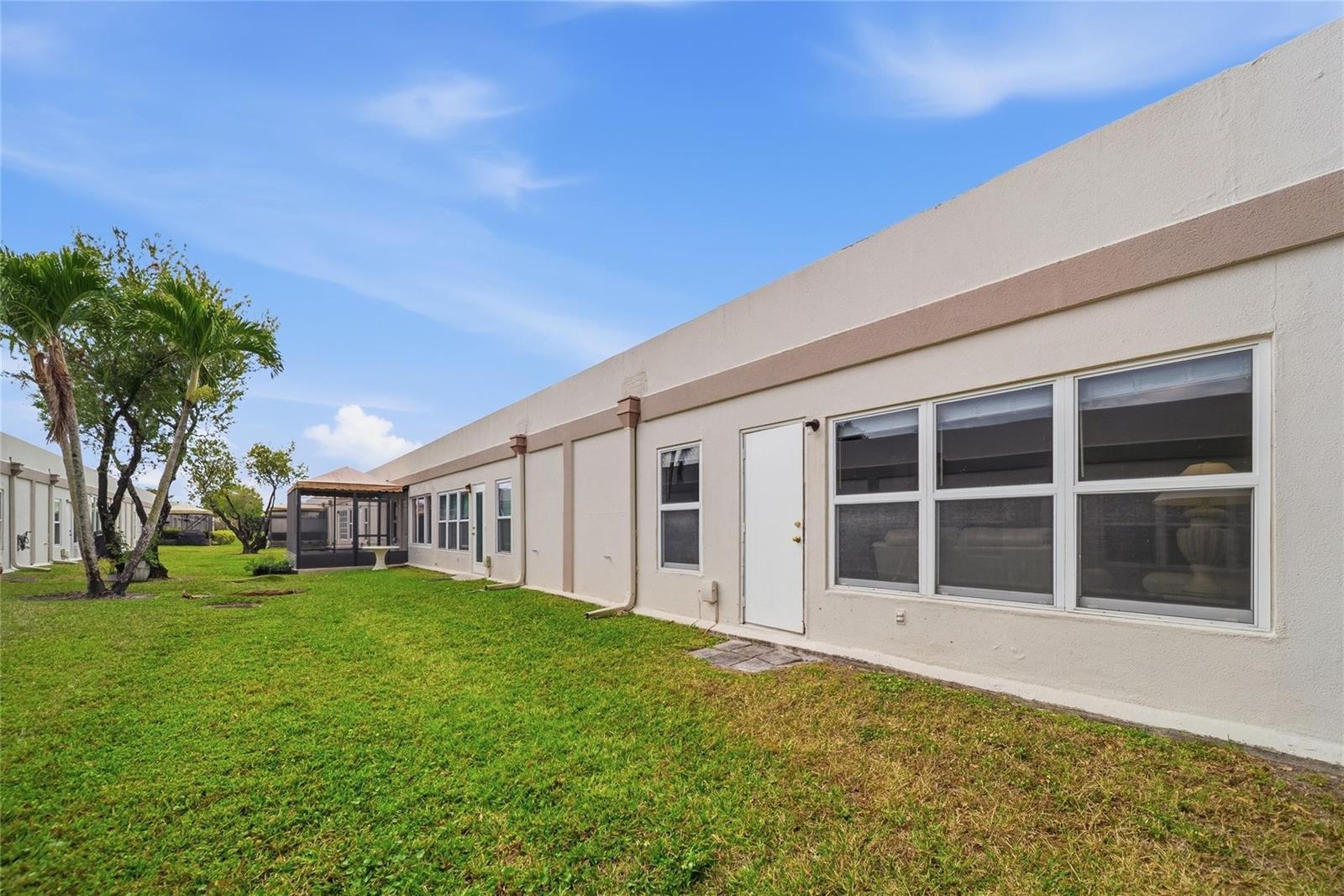 A long, single-story stucco building with a white door and windows overlooks a grassy lawn — 18730 Stewart Circle # 7, Boca Raton FL 33496, BOCA RATON, FL