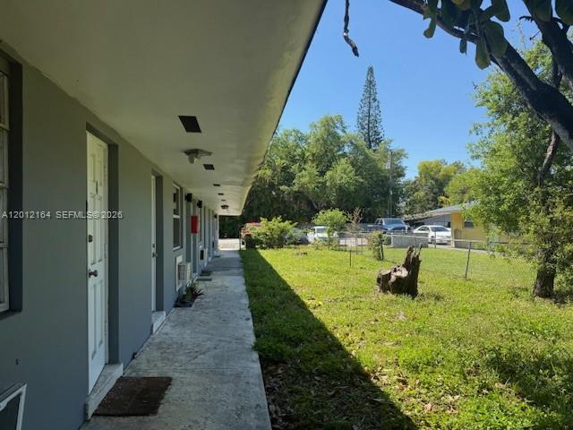 A concrete walkway runs along the exterior of a gray building beside a grassy yard — 151 NW 164th ST, Miami FL 33169, MIAMI, FL