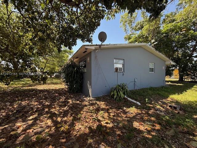 The exterior of a gray, single-story house is surrounded by trees and fallen leaves — 151 NW 164th ST, Miami FL 33169, MIAMI, FL