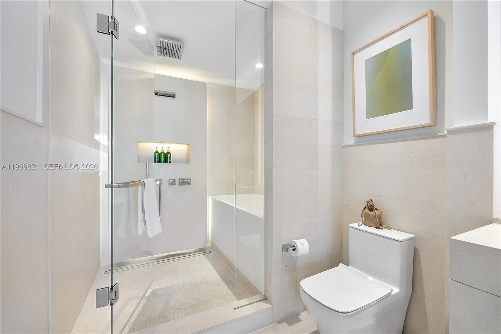 A modern bathroom features a glass-enclosed shower, a white toilet, and light-colored stone tile walls — 102 24th St # 1612, Miami Beach FL 33139, MIAMI BEACH, FL