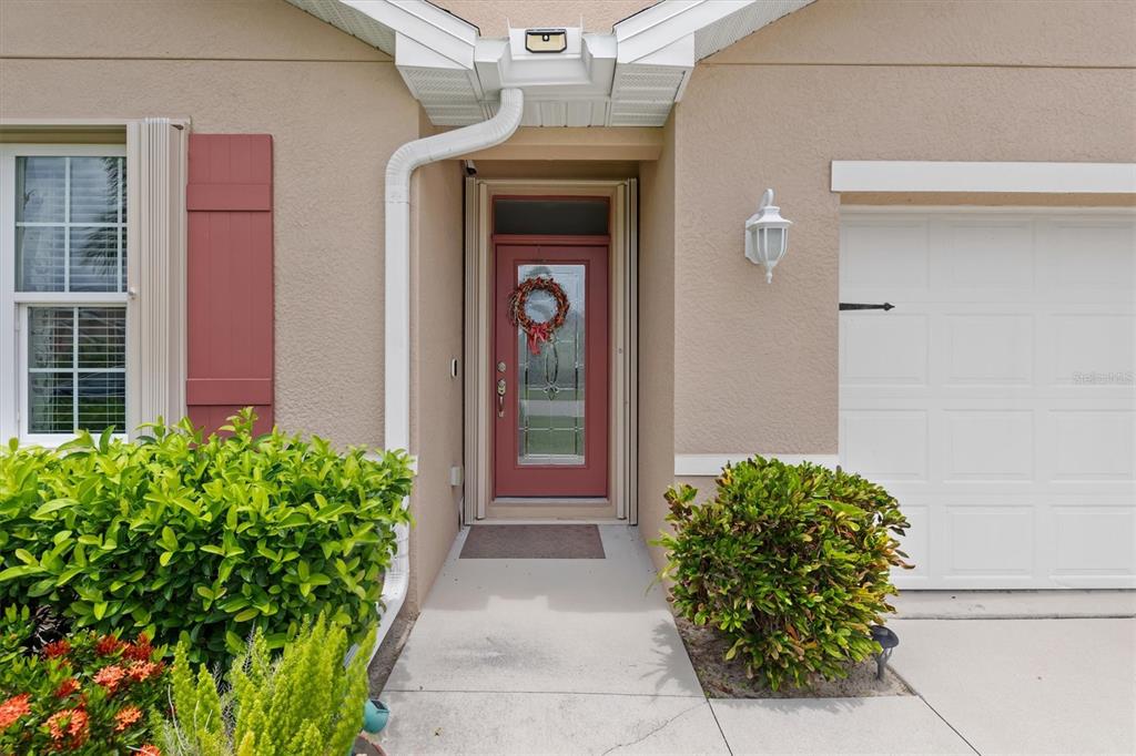 The exterior of a home features a red front door, a garage, and landscaping — 7436 MIKASA DRIVE, PUNTA GORDA, FL