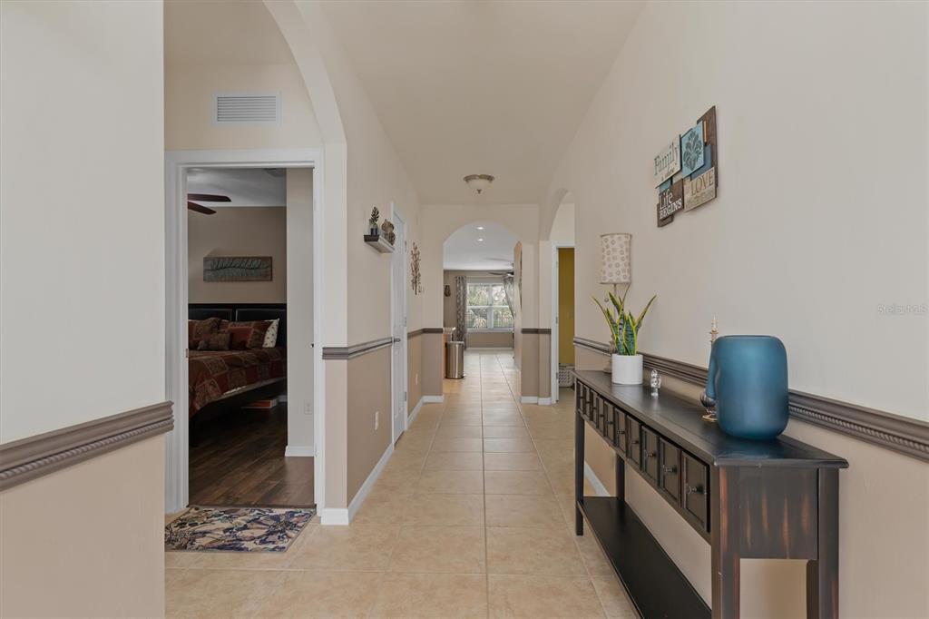 A tiled hallway leads past a bedroom entrance toward an arched opening at the end — 7436 MIKASA DRIVE, PUNTA GORDA, FL