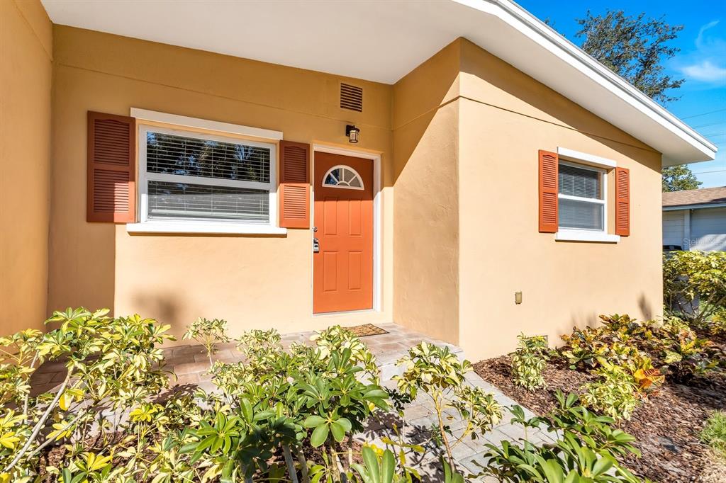 The exterior of a house features a tan stucco wall, an orange front door, and shutters — 5813 27TH AVENUE S, GULFPORT, FL