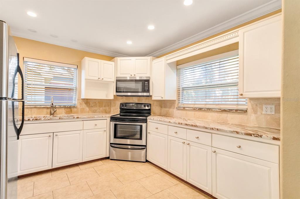 A kitchen with white cabinets, stainless steel appliances, and tan tile countertops and flooring — 5813 27TH AVENUE S, GULFPORT, FL