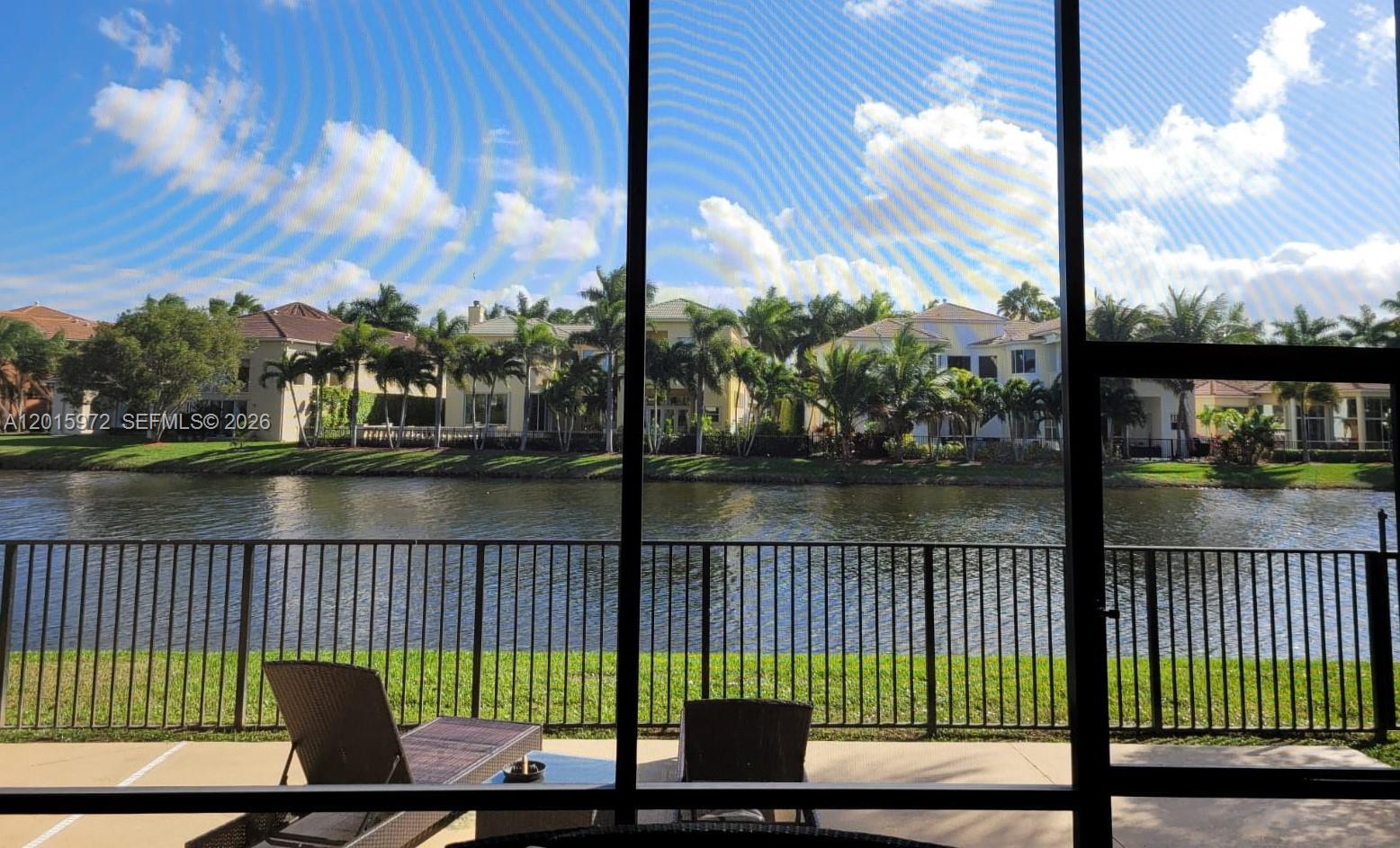 A view of a lake and houses from a screened-in patio with outdoor furniture — 2574 Treanor Ter, Wellington FL 33414, WELLINGTON, FL