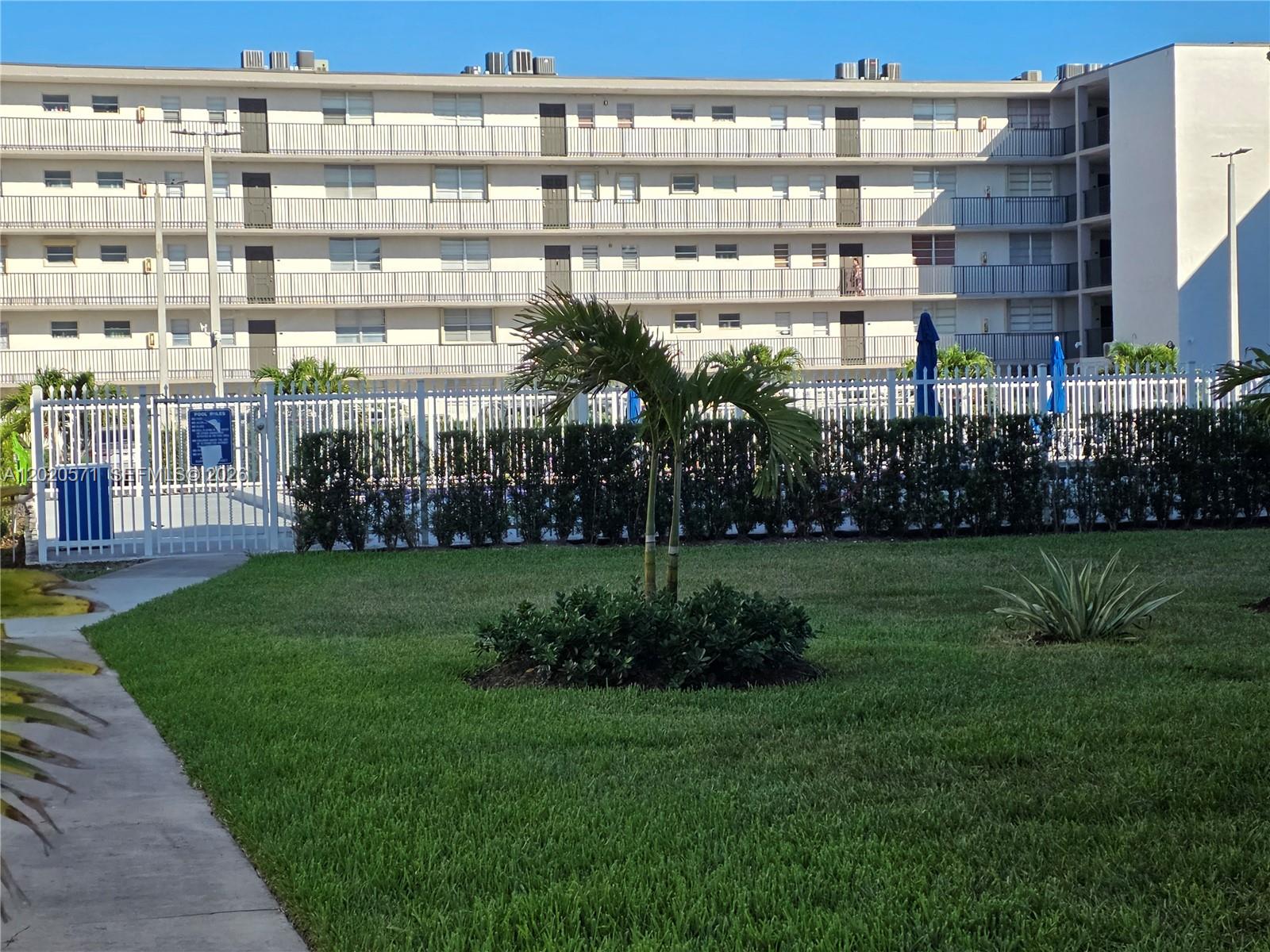 A multi-story apartment building sits behind a white fence, a lawn, and a palm tree — 14150 SW 84th St # I, Miami FL 33183, MIAMI, FL