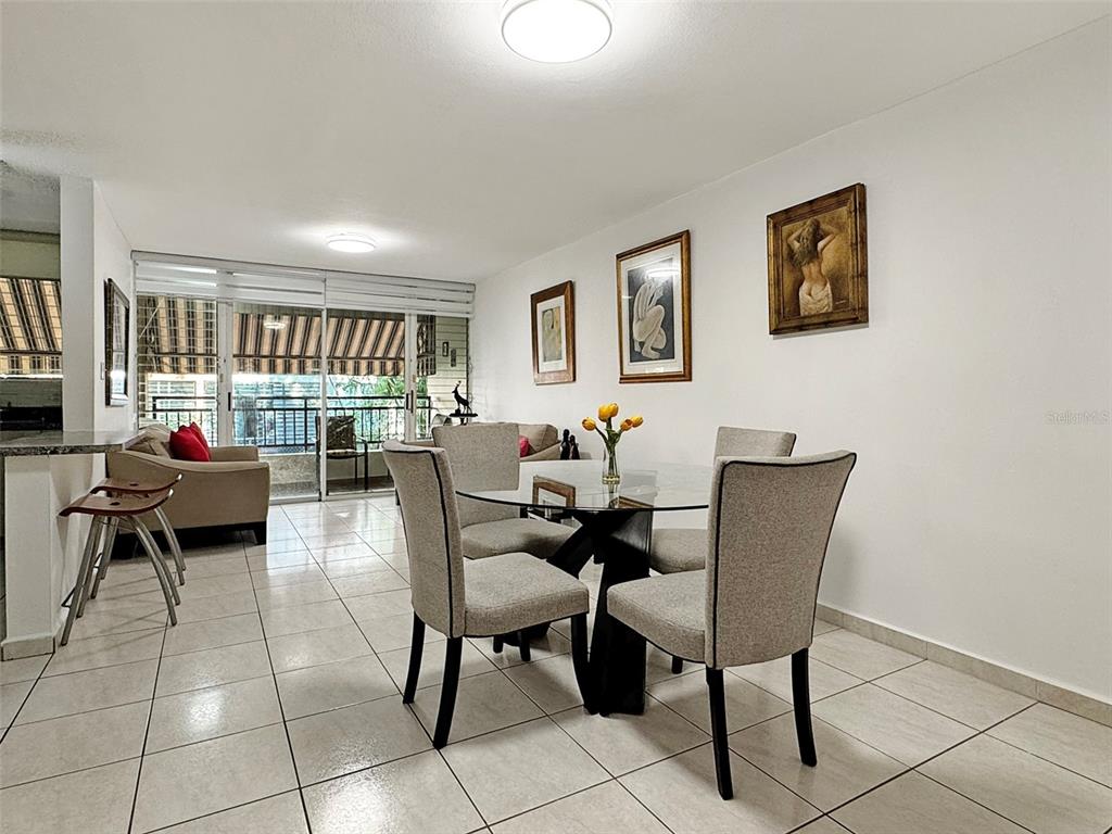 A dining area with a glass table, four chairs, and tiled floors leads to a balcony — Cond Valles de Torrimar BLVD. PEDRO FULLANA VIRELLA UNIT D-212, GUAYNABO, PR