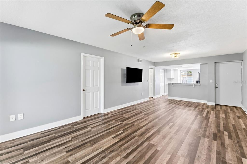 A living room with gray walls, wood-look flooring, a ceiling fan, and an open kitchen — 126 CYPRESS COURT UNIT 26, OLDSMAR, FL