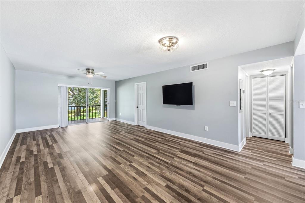 An empty living room features light gray walls, wood-look flooring, a ceiling fan, and a balcony — 126 CYPRESS COURT UNIT 26, OLDSMAR, FL